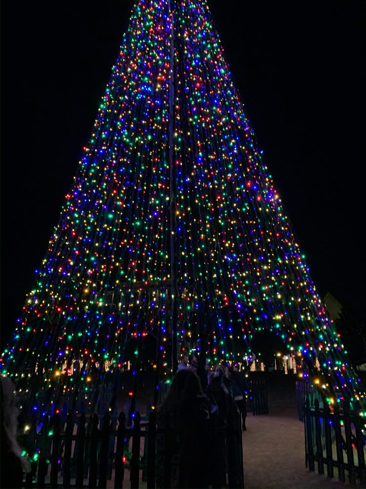 Tall cone-shaped structure covered in colorful Christmas lights at night.