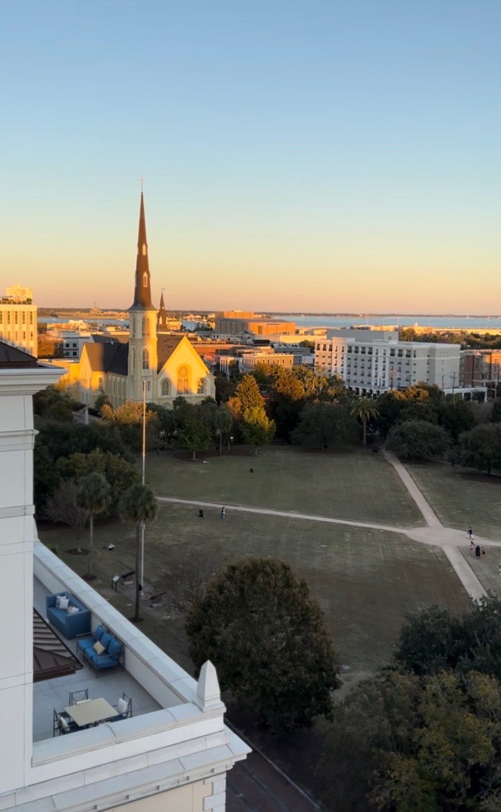 Park view with church steeple, buildings, and sunset in the background.